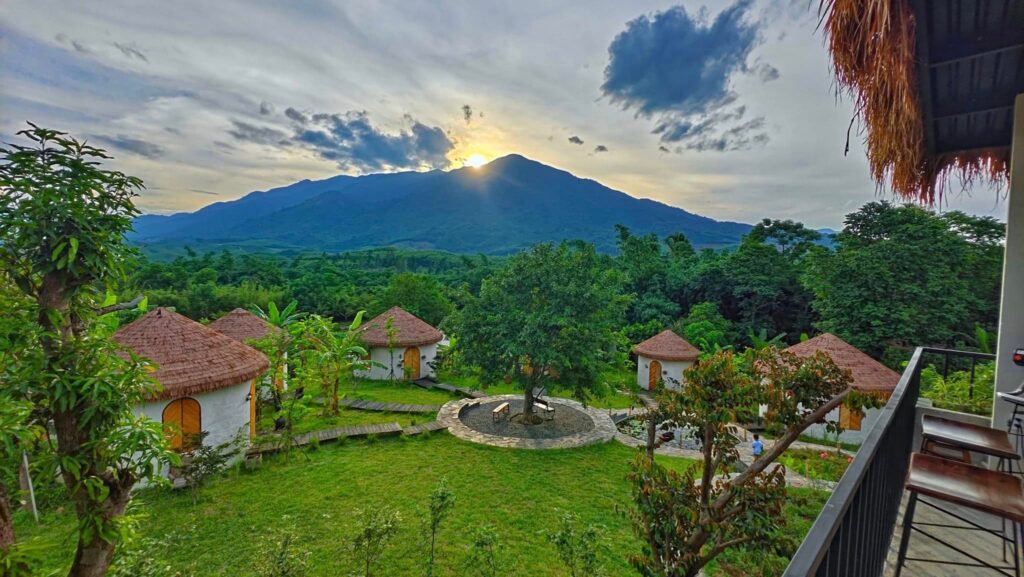 Cảnh hoàng hôn buông xuống khu nhà mái rơm nhân tạo, với núi non phía xa.