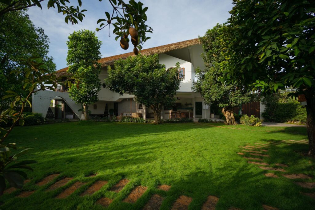 Khuôn viên sân vườn biệt thự nghỉ dưỡng với mái nhà sử dụng rơm nhân tạo, bao quanh bởi cây xanh tự nhiên.