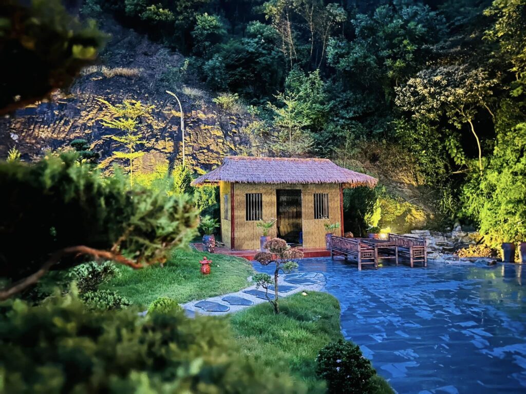 Nhà nghỉ trong vườn chùa sử dụng tường tre nhân tạo và mái rơm, nổi bật dưới ánh đèn đêm